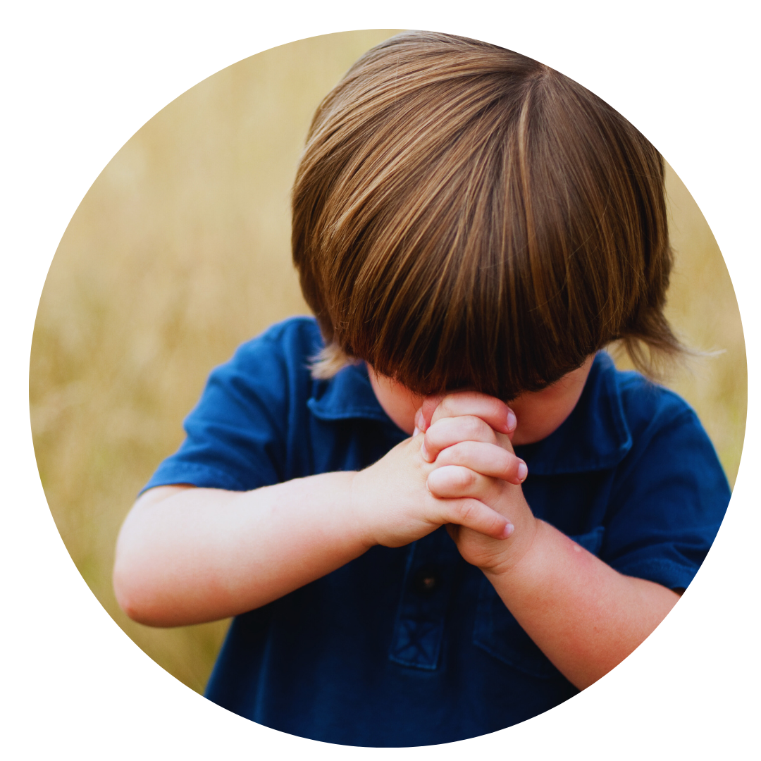 menino rezando com a cabeça baixa. Veste camisa azul e tem cabelo castanho liso.